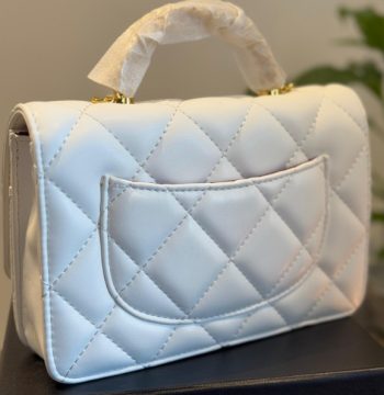 Chanel Mini Top Handle Flap Bag in white lambskin leather with gold-tone hardware, featuring classic quilting, a CC turn-lock closure, and a versatile top handle design.