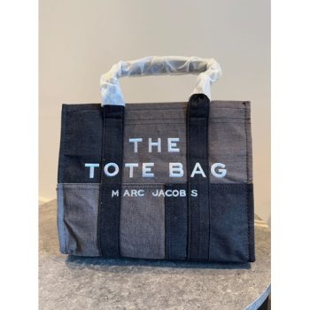 Marc Jacobs The Denim Tote Bag in black denim featuring a bold logo, spacious interior, top-zip closure, and detachable shoulder strap.